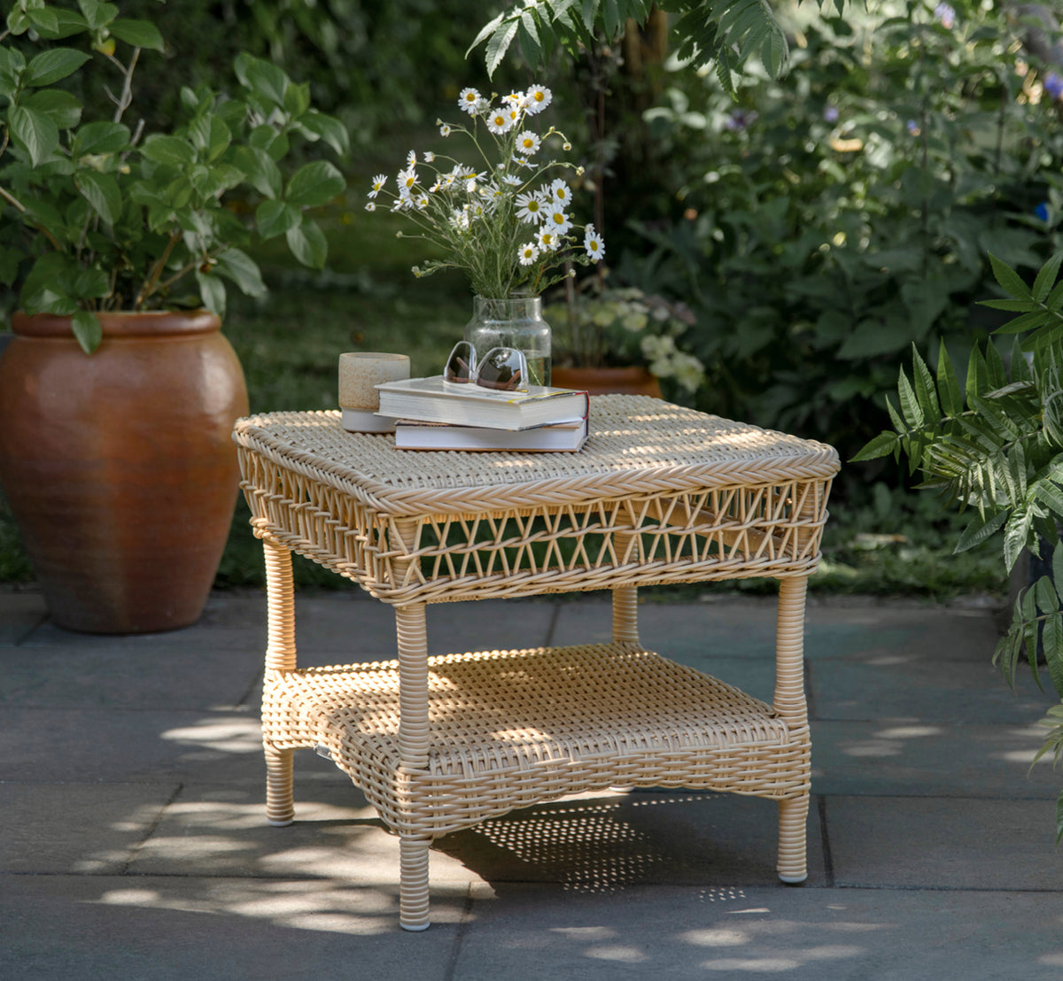 Dette er et livsstilsbillede af Susy Sidebord i natural ArtFibre Aluminium, på en kystterrasse med havudsigt, strandgræs og hvide søjler.