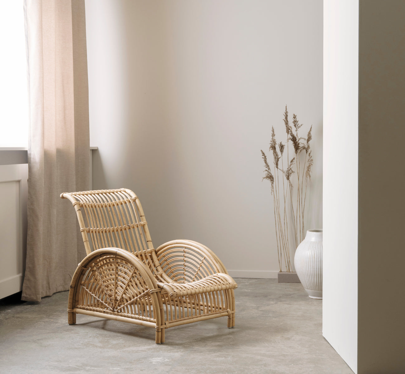Dette er et livsstilsbillede af Paris Lænestol i polished natural rattan. Placeret på et sildebensparketgulv ved siden af en matchende bænk.