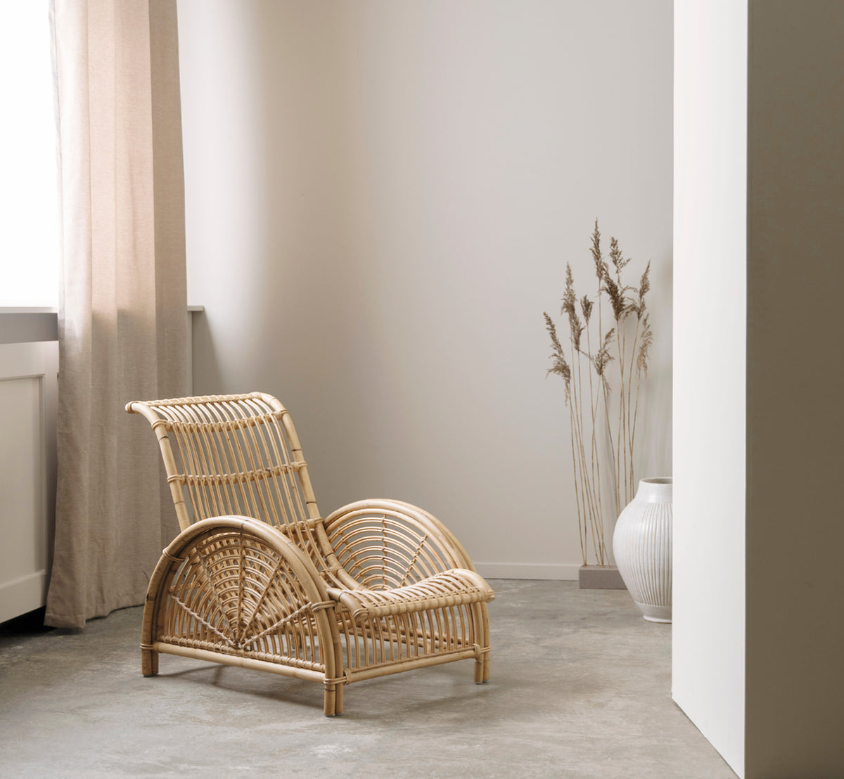 Dette er et livsstilsbillede af Paris Lænestol i polished natural rattan. Placeret på et sildebensparketgulv ved siden af en matchende bænk.