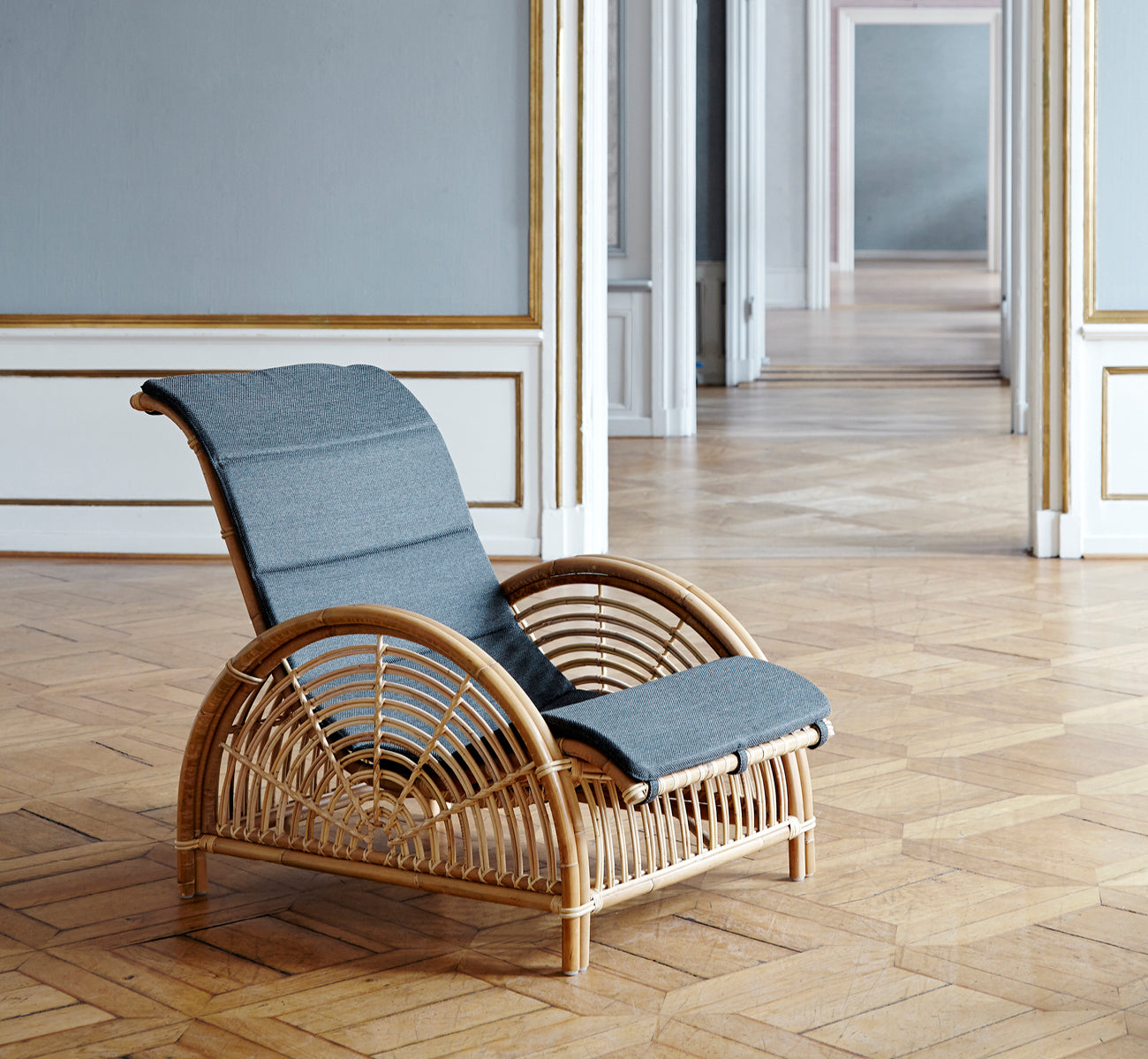 Dette er et livsstilsbillede af Paris Lænestol i polished natural rattan. Placeret på et sildebensparketgulv ved siden af en matchende bænk.