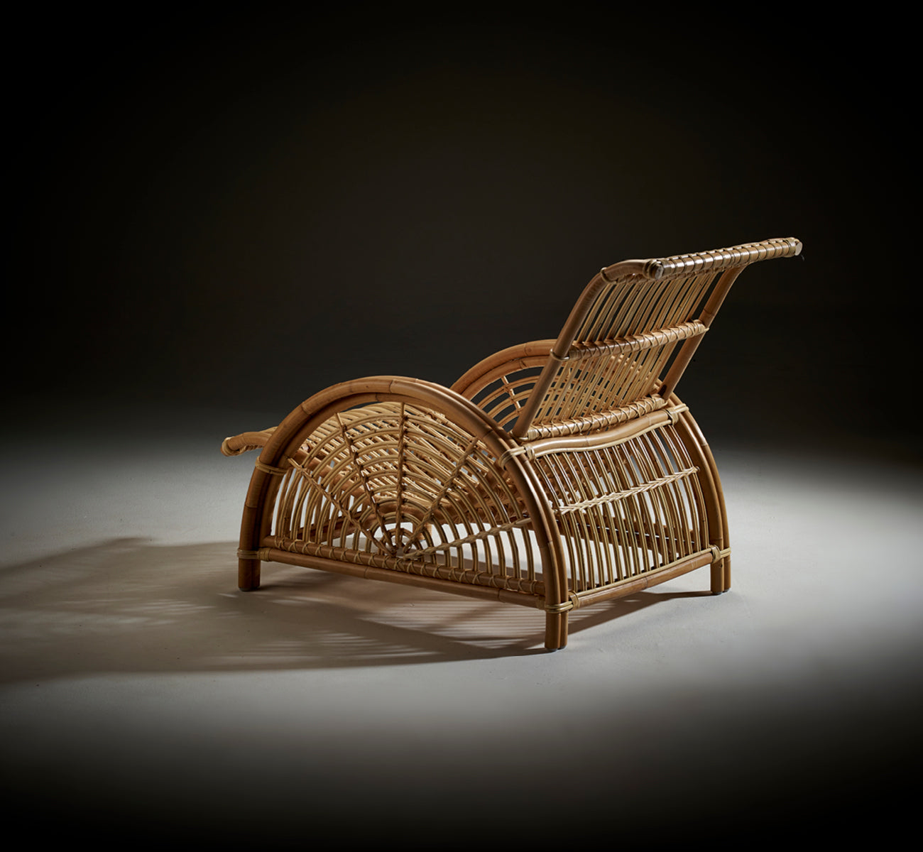 Dette er et livsstilsbillede af Paris Lænestol i polished natural rattan. Placeret på et sildebensparketgulv ved siden af en matchende bænk.