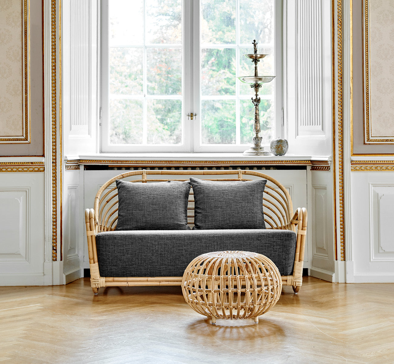 Dette er et livsstilsbillede af Charlottenborg Sofa i polished Natural Rattan, i et elegant klassisk interiør med forseggjorte forgyldte stukdetaljer.