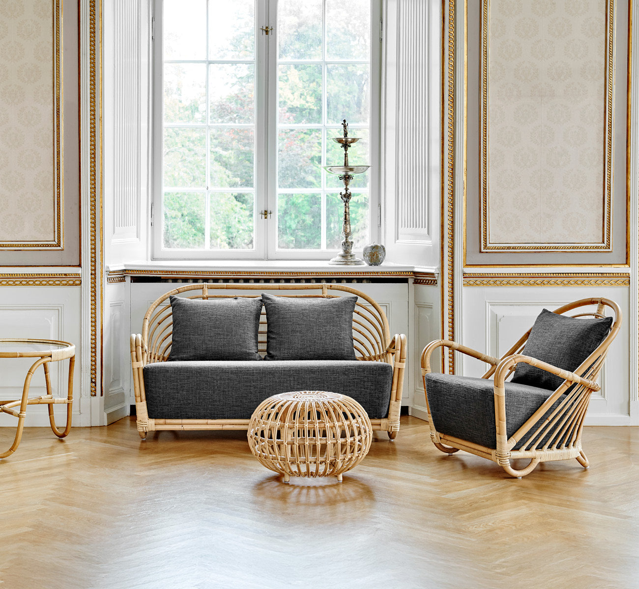 Dette er et livsstilsbillede af Charlottenborg Sofa i polished Natural Rattan, i et elegant klassisk interiør med forseggjorte forgyldte stukdetaljer.