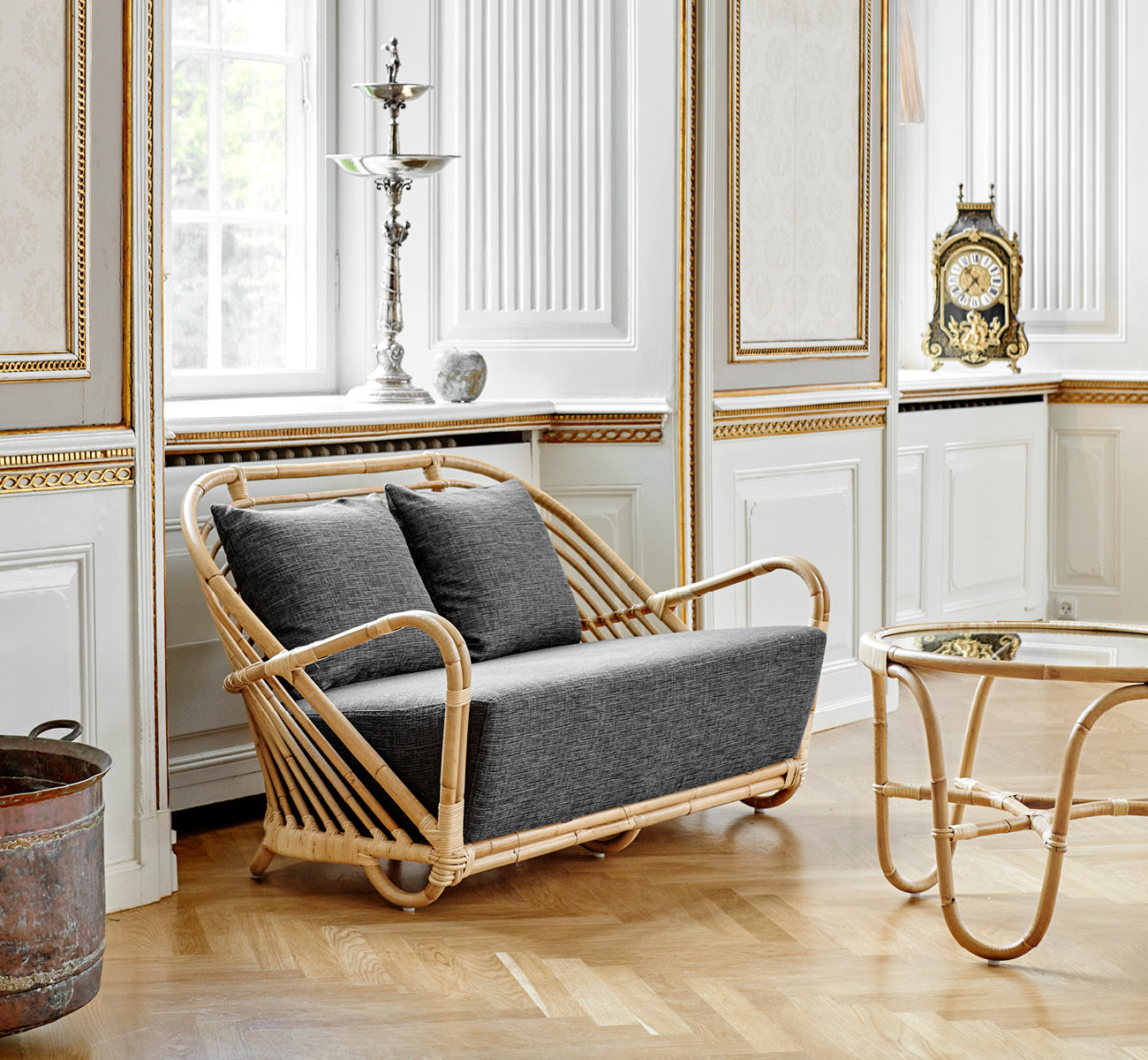 Dette er et livsstilsbillede af Charlottenborg Sofa i polished Natural Rattan, i et elegant klassisk interiør med forseggjorte forgyldte stukdetaljer.