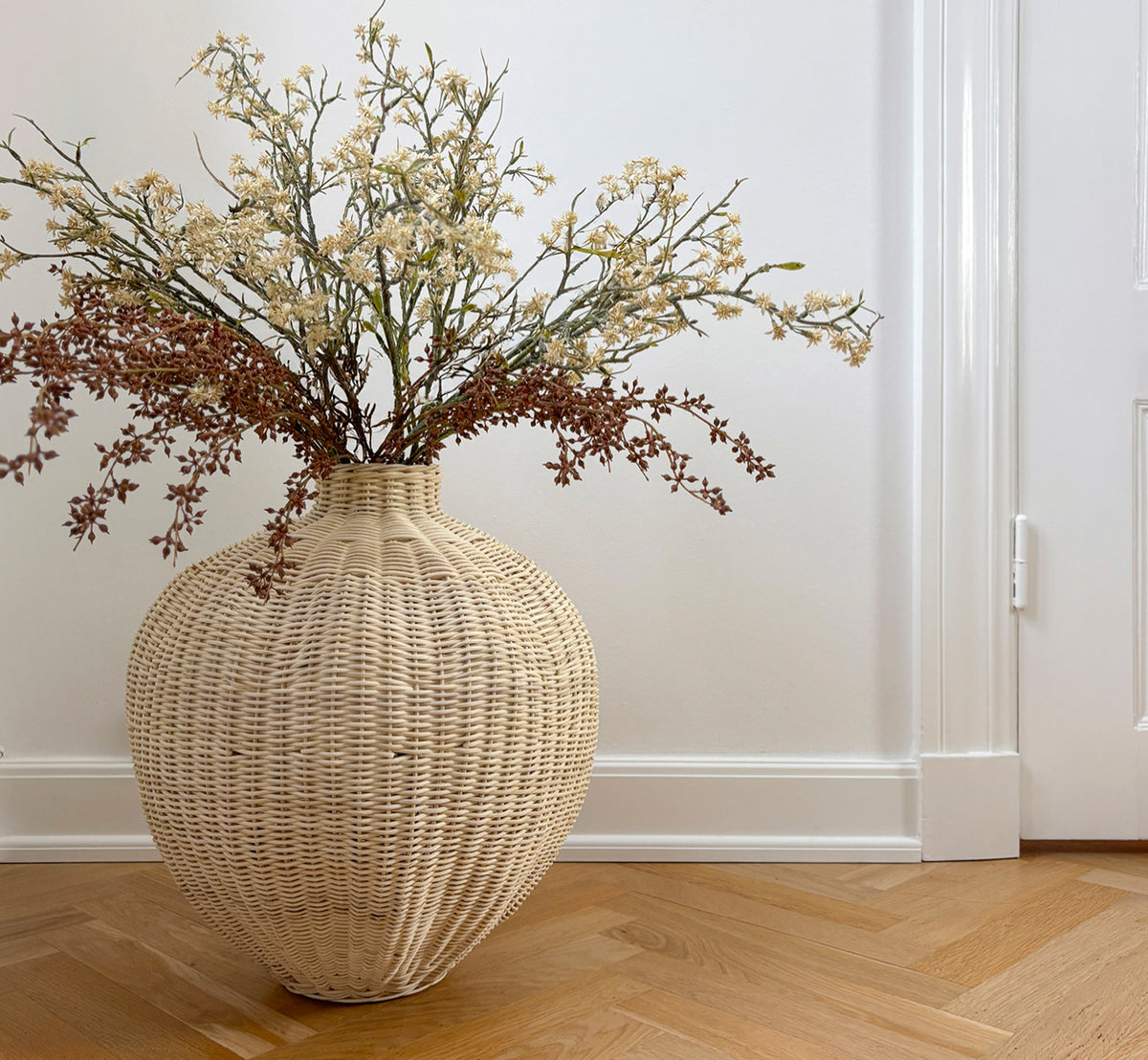 Dette er et livsstilsbillede af Flumen Kurv i natural core weave iron frame, i et lyst hvidt interiør med lambrisering, stylet med tørrede blomster.