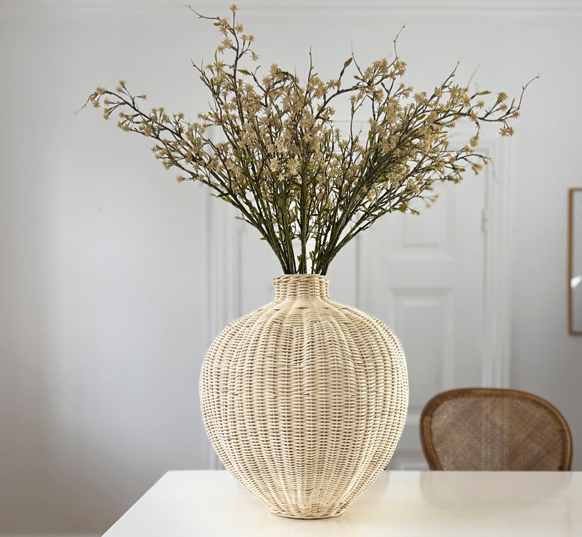 Dette er et livsstilsbillede af Flumen Kurv i natural core weave iron frame, i et lyst hvidt interiør med lambrisering, stylet med tørrede blomster.