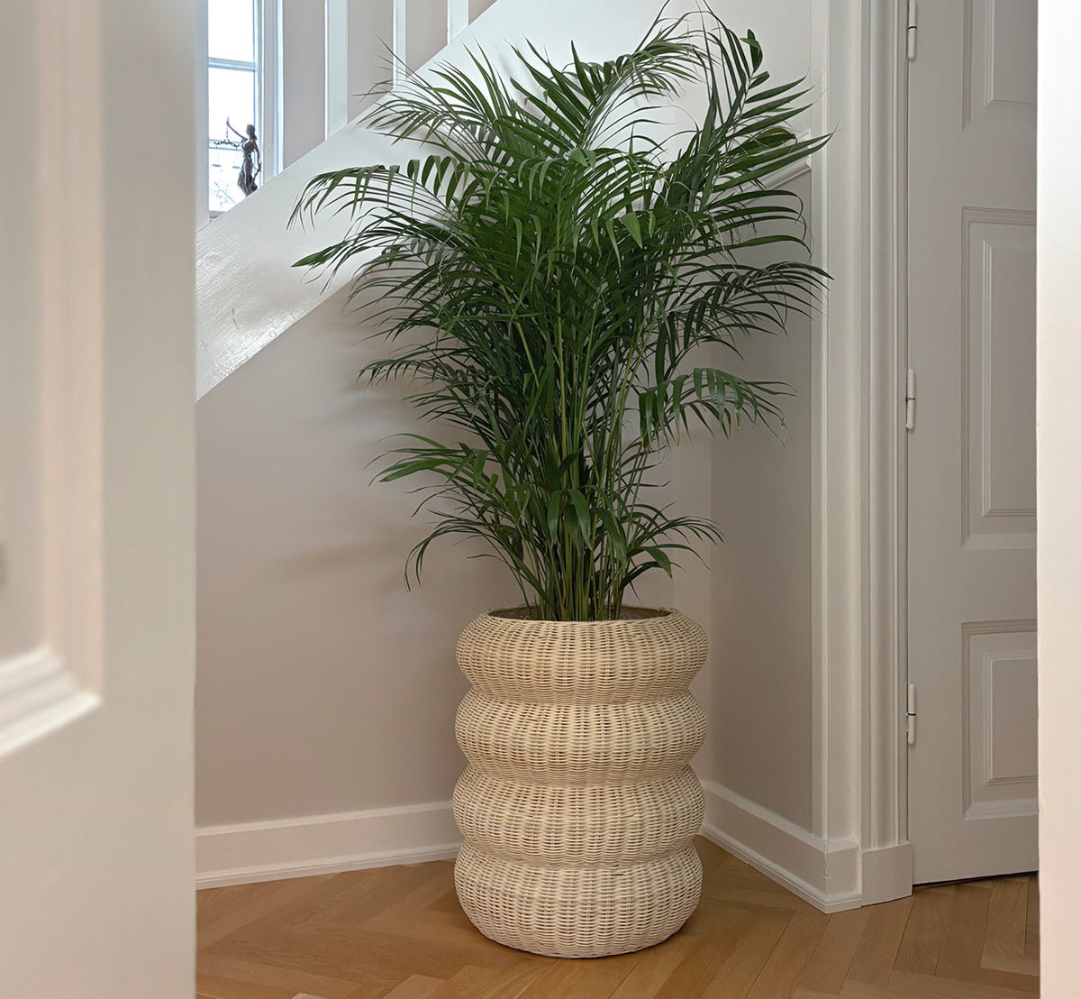 Dette er et livsstilsbillede af Mel Basket i natural core weave rattan frame. På sildebensgulv i en lys panelbeklædt entre.