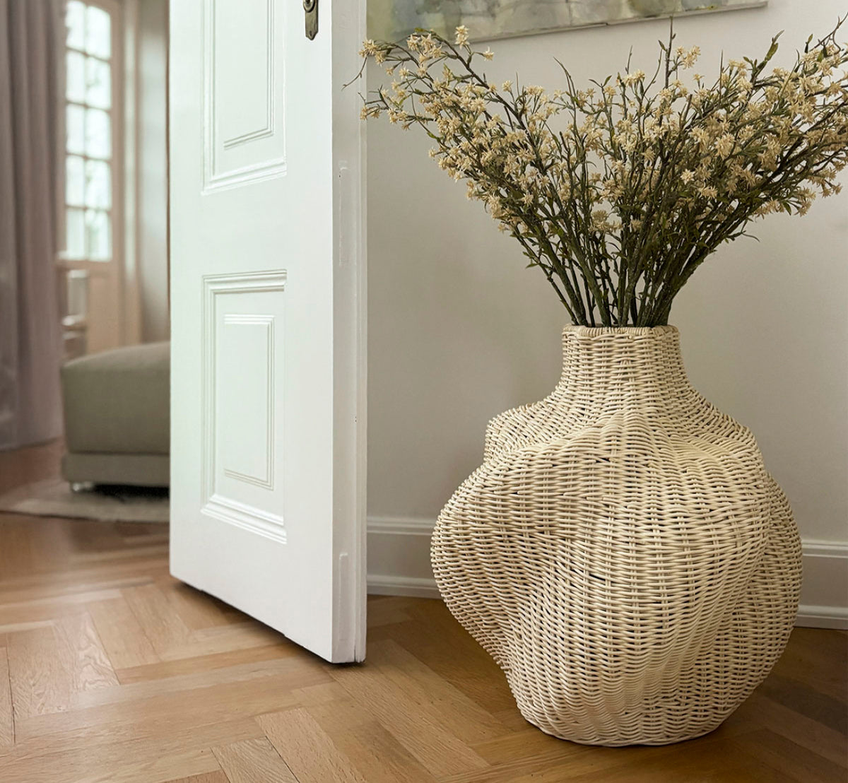 Dette er et livsstilsbillede af Solaris Basket Ø46 cm i natural core weave iron frame. Stylet med tørrede blomster ved siden af en hvid dør på et parketgulv.