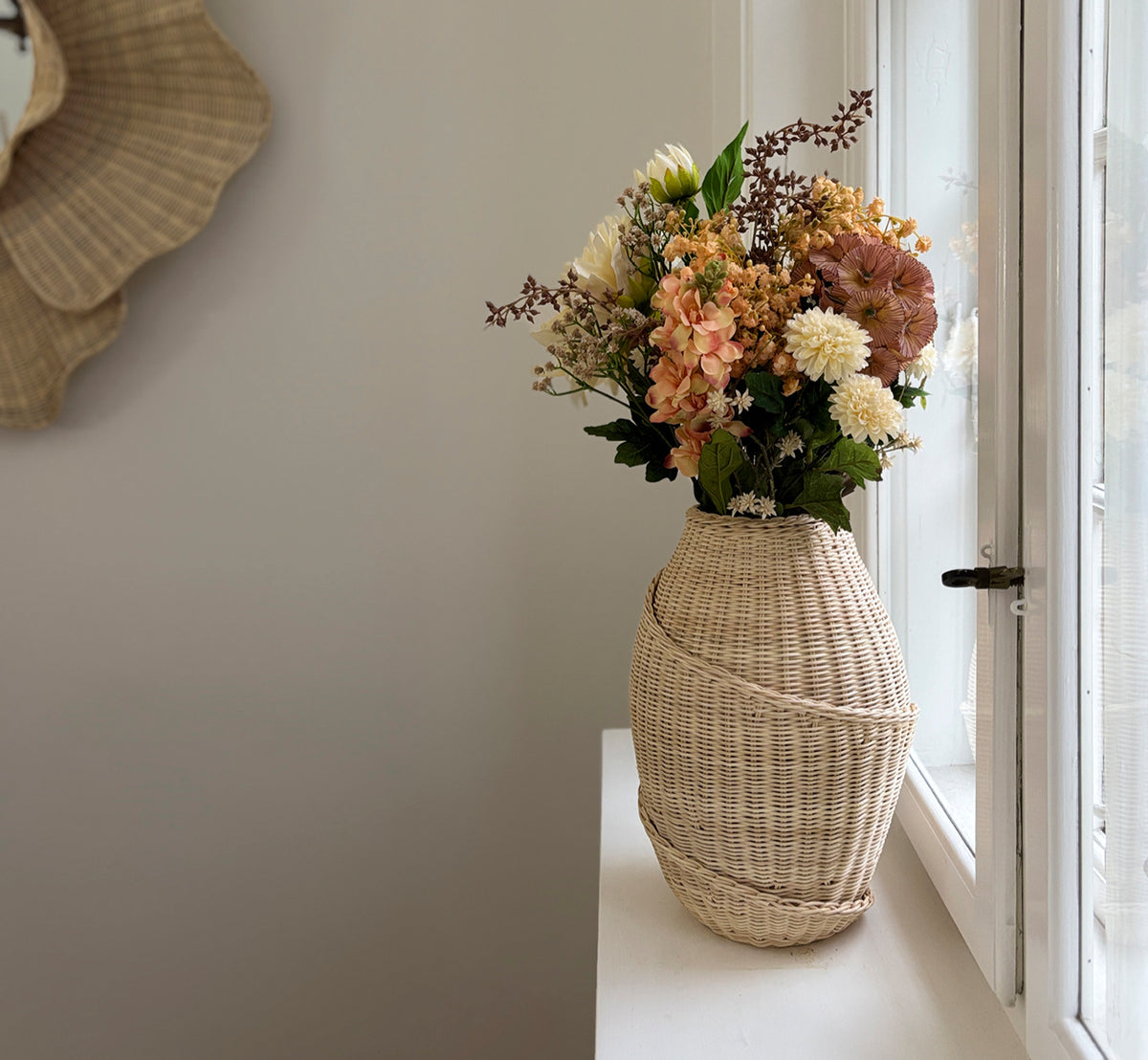 Dette er et livsstilsbillede af Floris Kurv i natural core weave iron frame, i et lyst hvidt interiør med lambrisering, stylet med tørrede blomster.