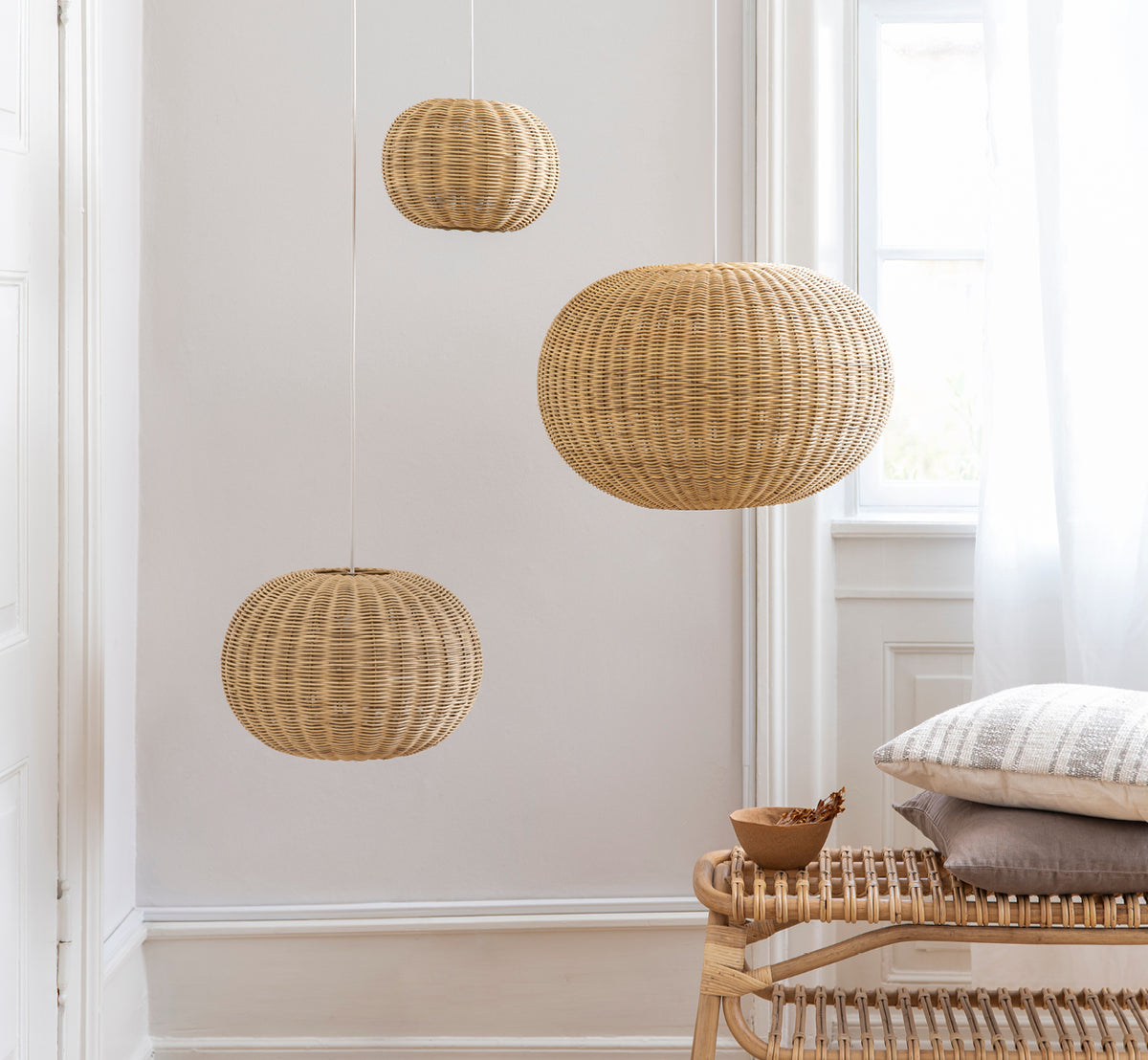 Dette er et livsstilsbillede af Tangelo Lampshade Ø37 cm | Small i natural rattan. Tre pendler grupperet over en rattanbænk i et lyst interiør.