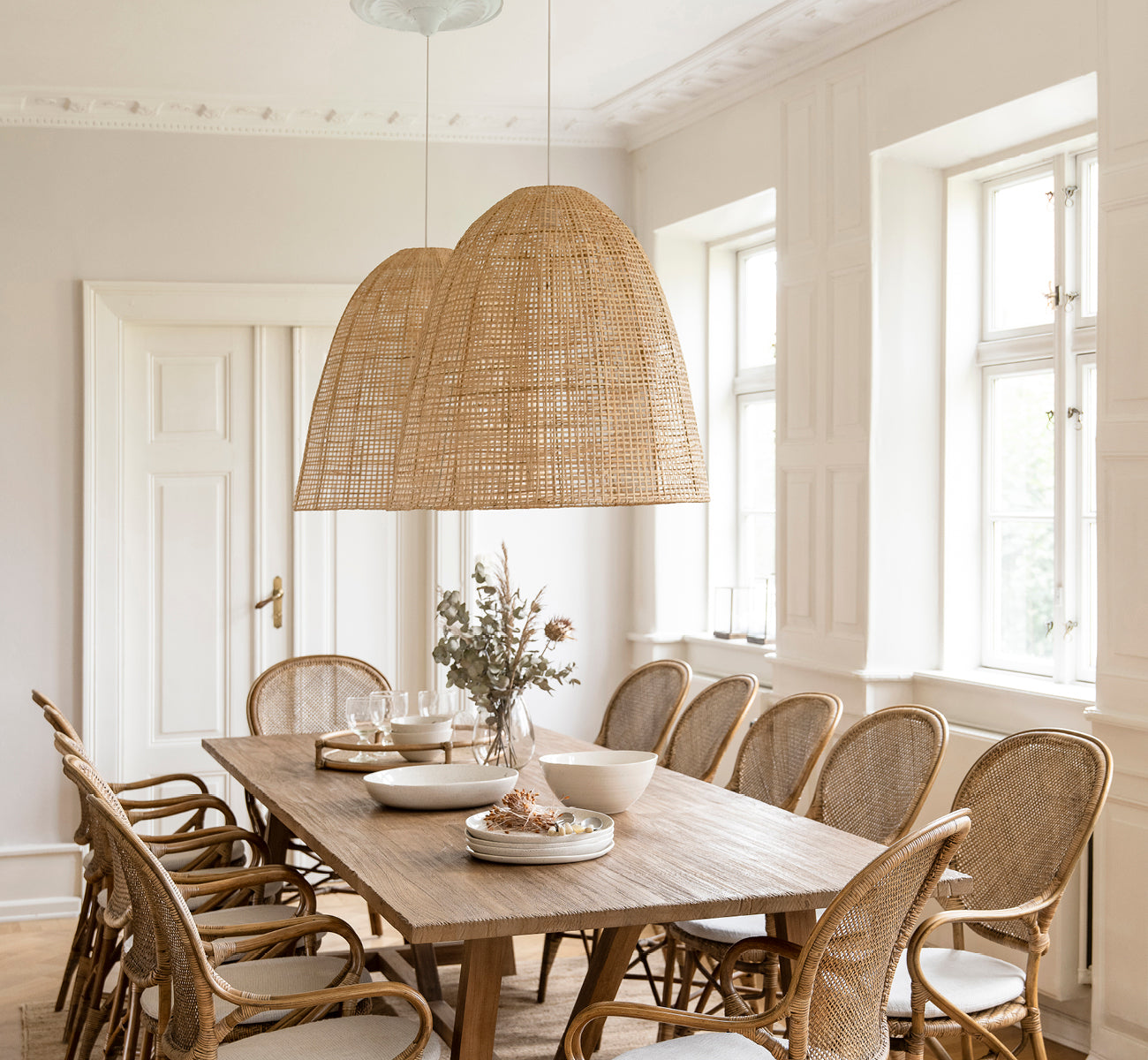 Dette er et livsstilsbillede af Showroom Lampeskærm i natural core weave artfibre & aluminium. Hængende over et dækket spisebord i et lyst rum.