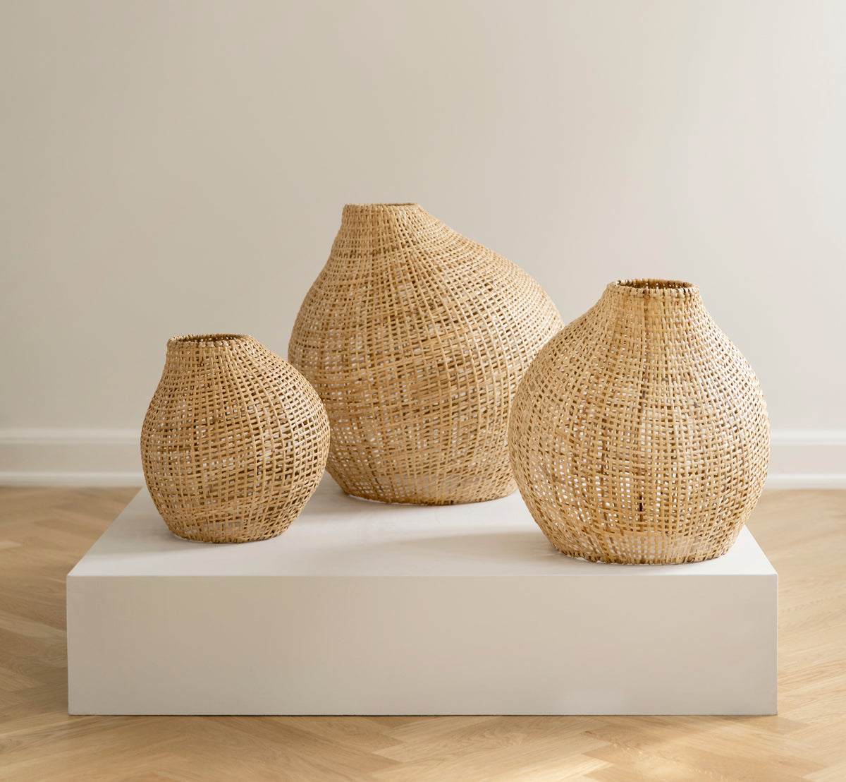 Dette er et livsstilsbillede af Figura Gulvlampeskærm i light natural weave rattan, udstillet på en hvid platform mod en neutral interiørbaggrund.