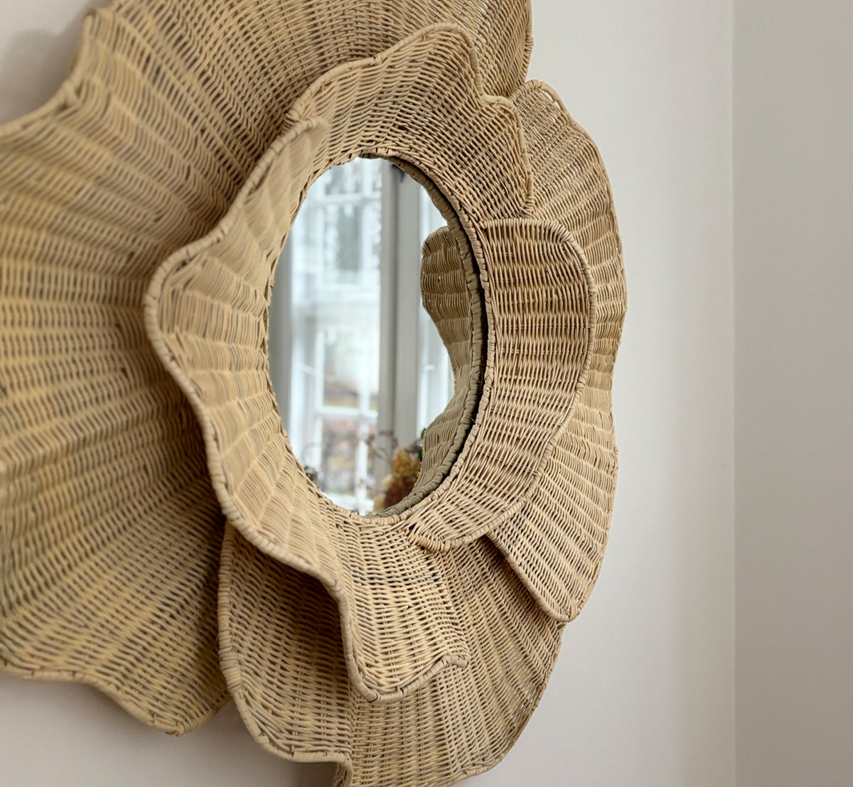 Dette er et livsstilsbillede af Floral Spejl i natural core weave iron frame, hængende i en lys spisestue med lysestager og naturligt vindueslys.