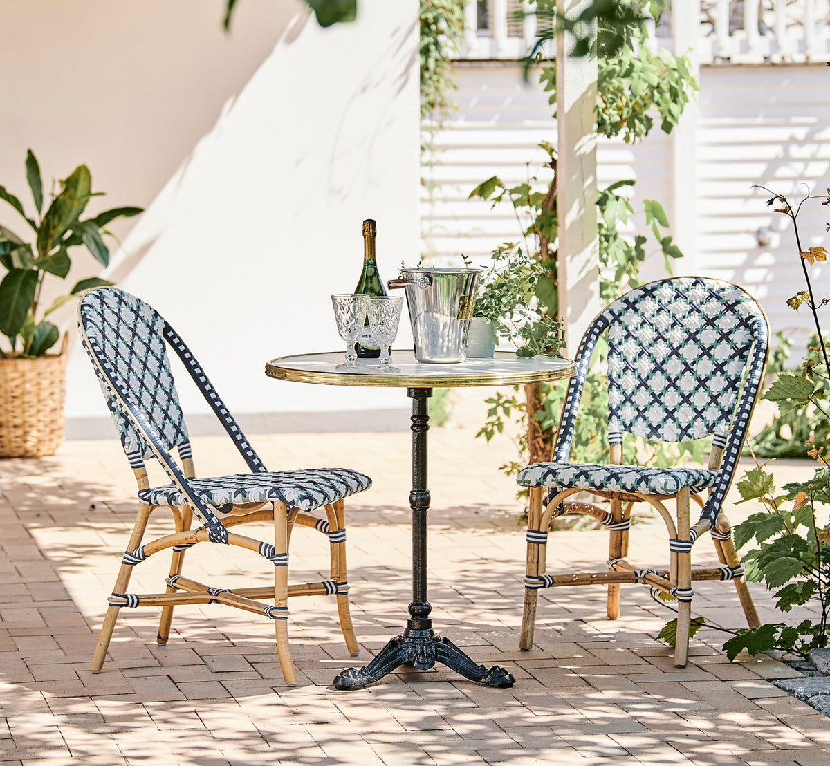 Dette er et livsstilsbillede af Lyon Cafébord Versalite Marble Ø70 cm i cast iron. Solrig terrasse med bistrostole og en champagneflaske.