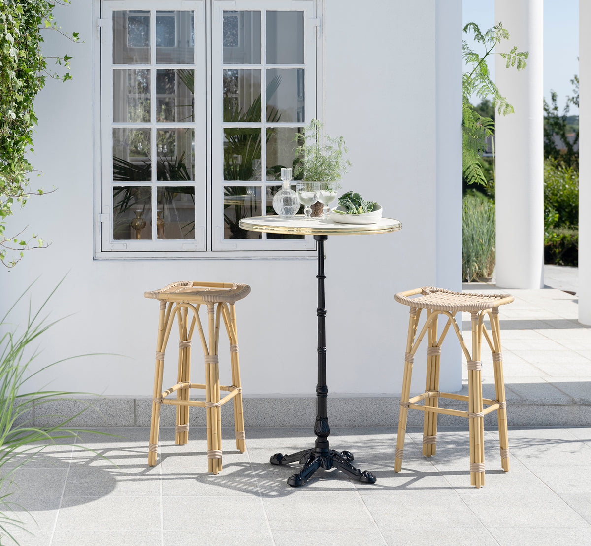 Dette er et livsstilsbillede af Lyon Barbord Versalite Marble Ø70 cm i cast iron. Elegant terrasse med barstole og grønne planter.