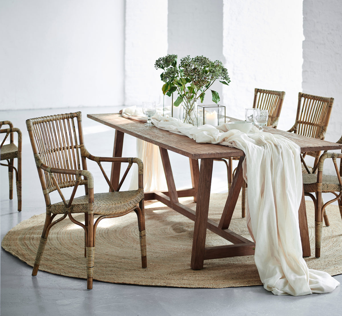 Dette er et livsstilsbillede af Jute Carpet Ø280 i grey jute. Under et spisebord med rattanstole, lindrapering og grønt.