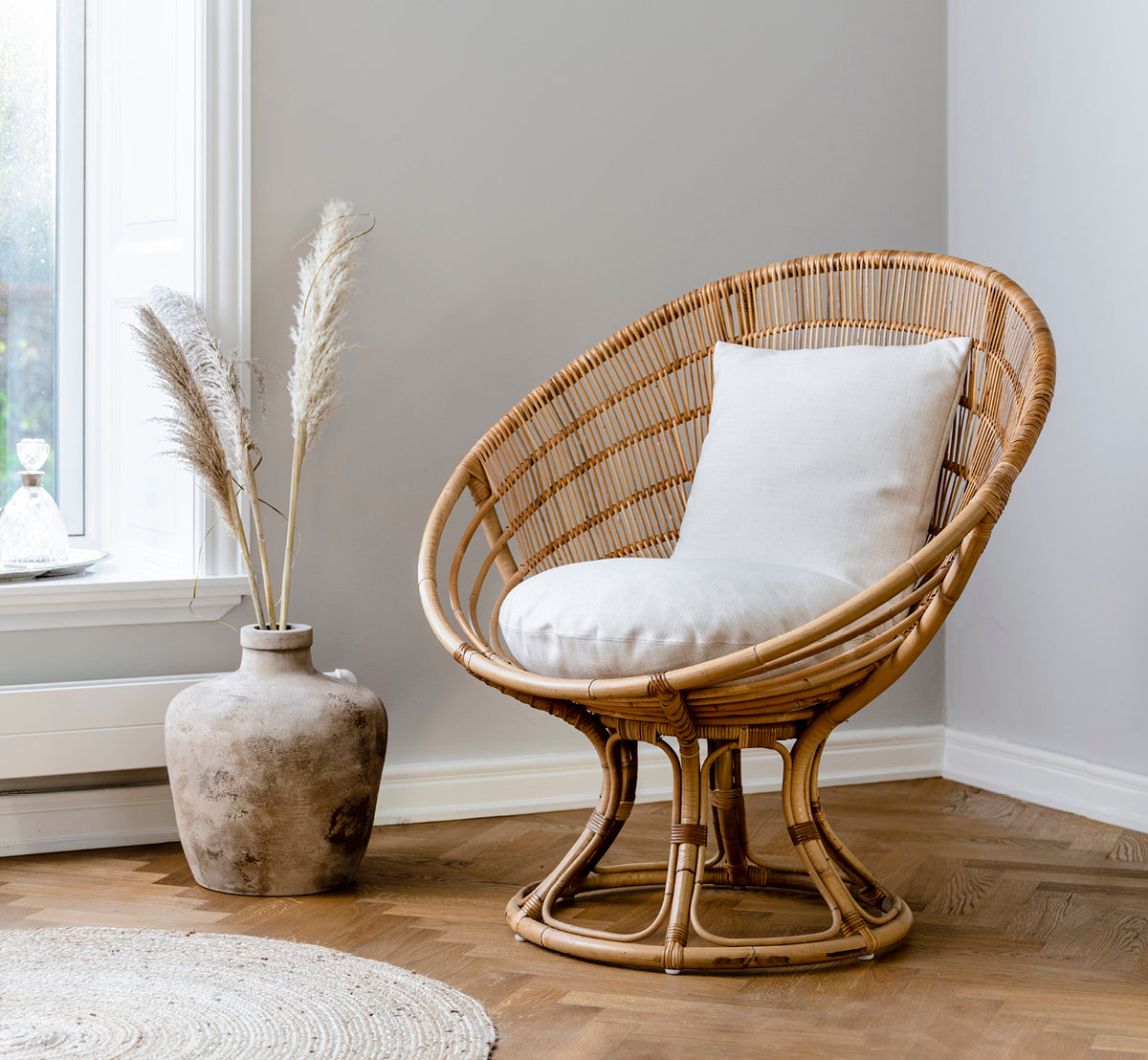 Dette er et livsstilsbillede af Luna Lænestol i natural skin on rattan. Stylet med en hvid pude i et hyggeligt hjørne med pampasgræsdekoration.