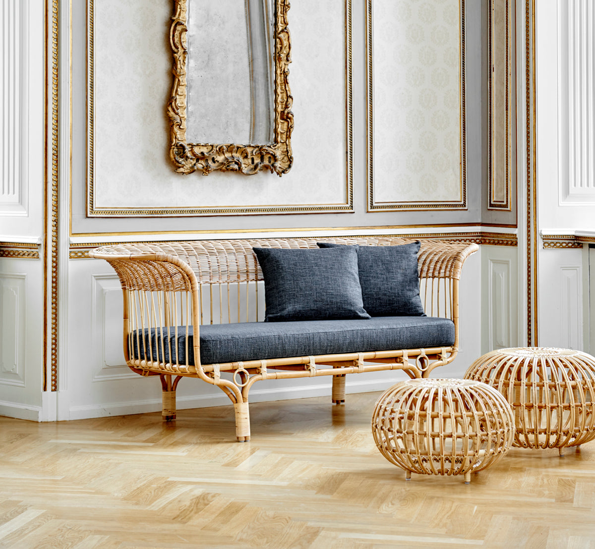 Dette er et livsstilsbillede af Ottoman Large i natural skin on rattan. Samlet i et klassisk panelinteriør med et forgyldt ur.