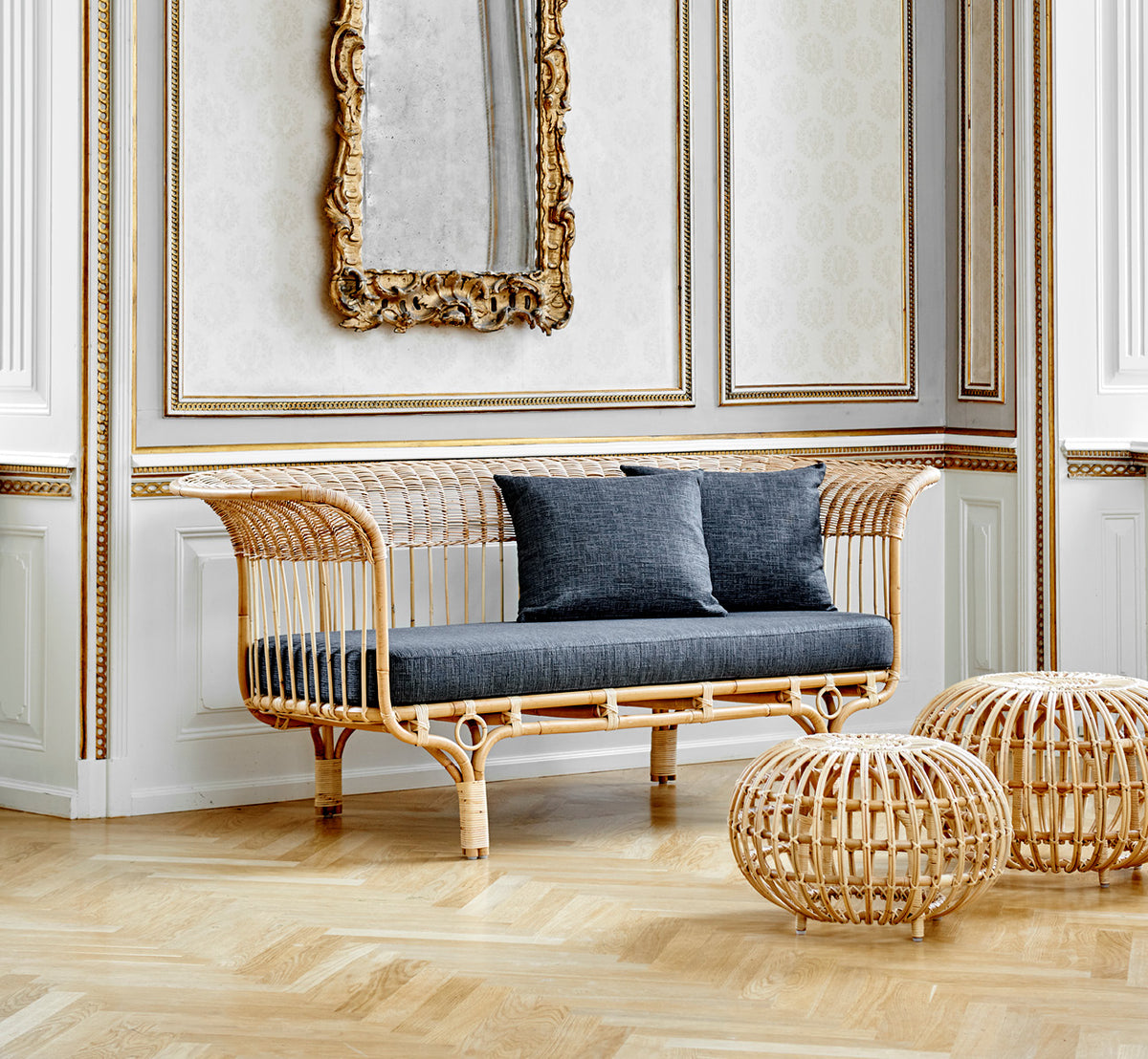 Dette er et livsstilsbillede af Belladonna Sofa i polished natural rattan, i et lyst skandinavisk interiør set gennem en hvid dørramme.