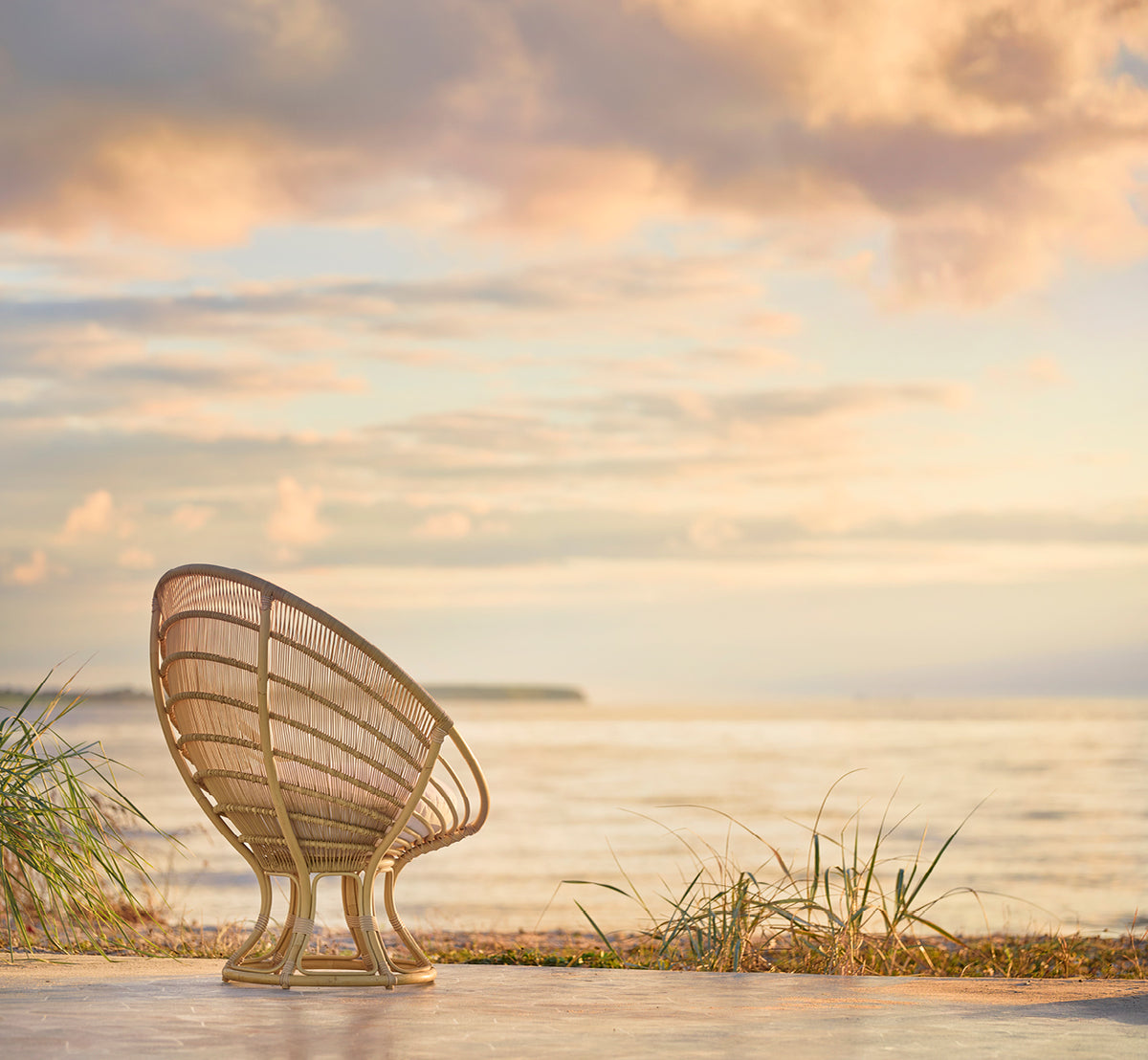 Dette er et livsstilsbillede af Luna Udendørs lænestol i natural aluminium artfibre. Set bagfra på en strand ved solnedgang med en pastelfarvet himmel.