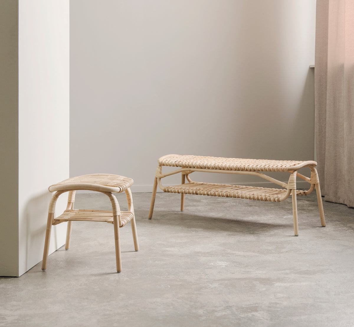 Dette er et livsstilsbillede af Machiya Bænk i natural skin on rattan. Minimalt rum med betongulv, rattanskammel og lingardin.