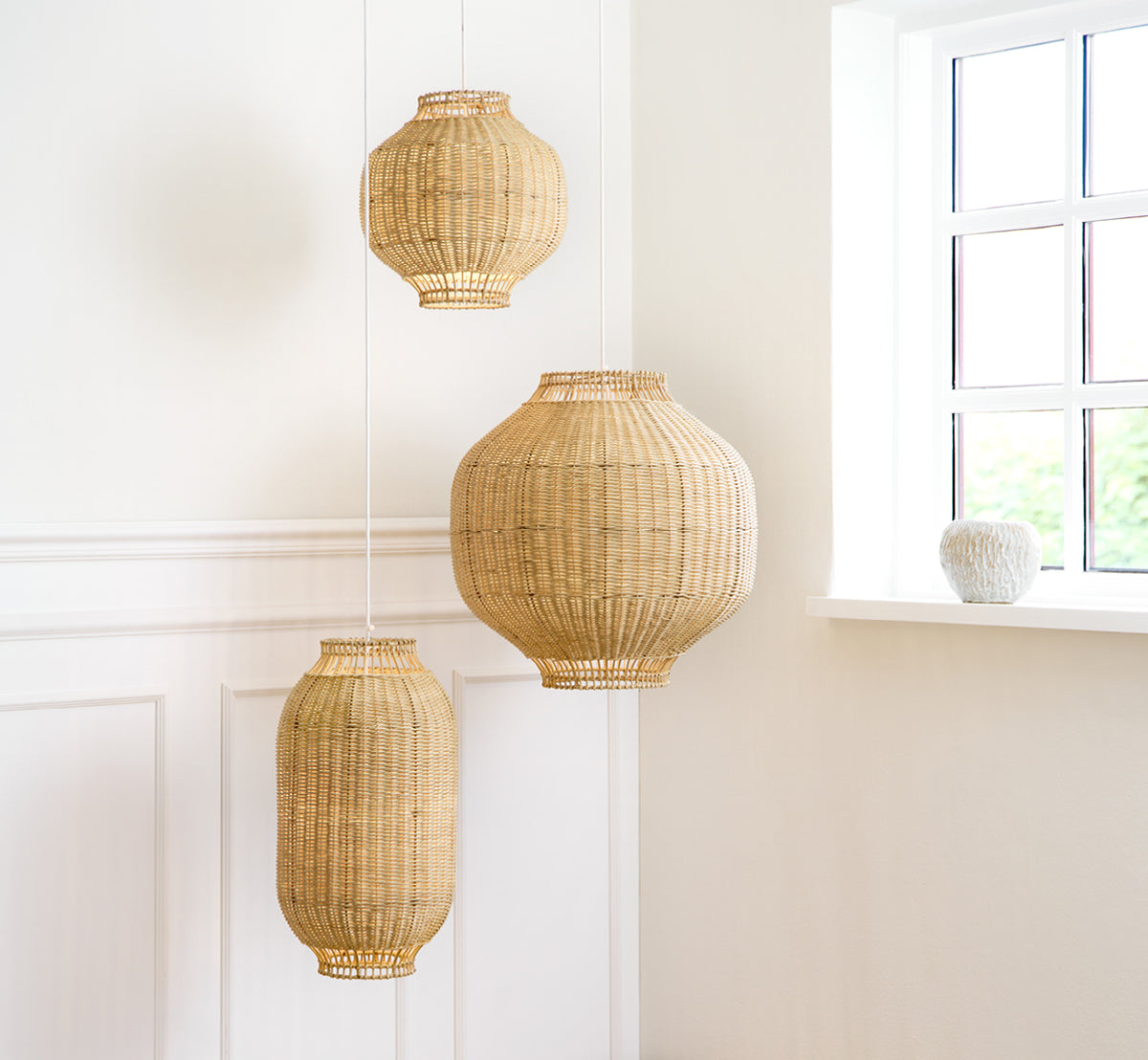 Dette er et livsstilsbillede af Tomori Lampeskærm i natural core weave rattan frame. Den største af tre pendler i et lyst panelrum.