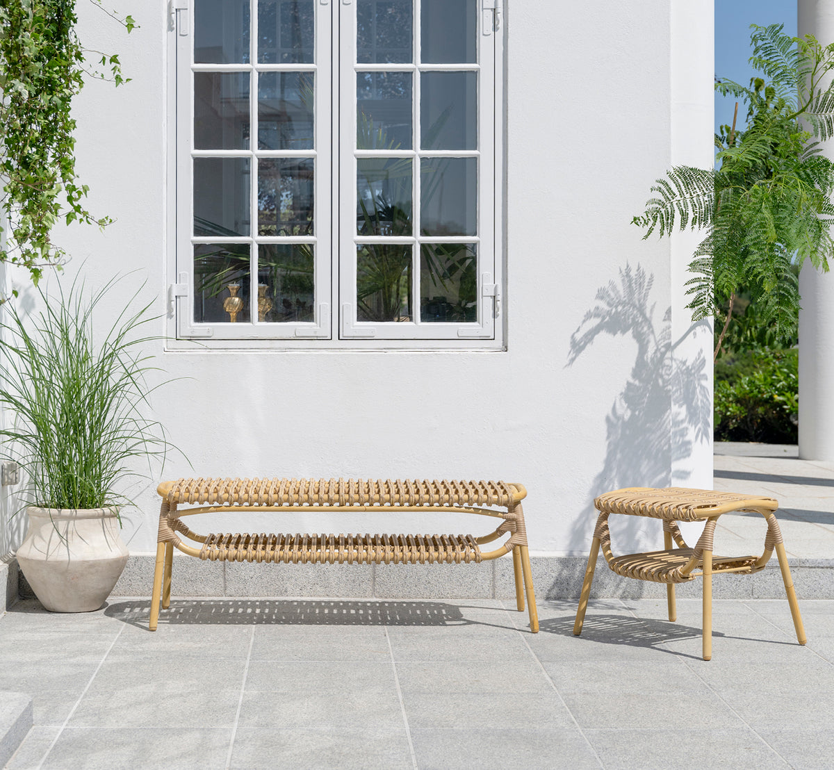 Dette er et livsstilsbillede af Machiya Udendørs bænk i natural aluminium artfibre. Hvid terrasse med udendørs skammel og grønne planter.