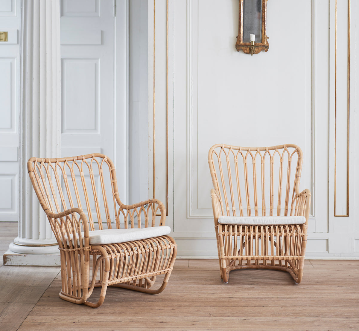 Dette er et livsstilsbillede af Tulip Lænestol i polished natural rattan. Kombineret med en matchende sofa i et lyst panelrum med dør.