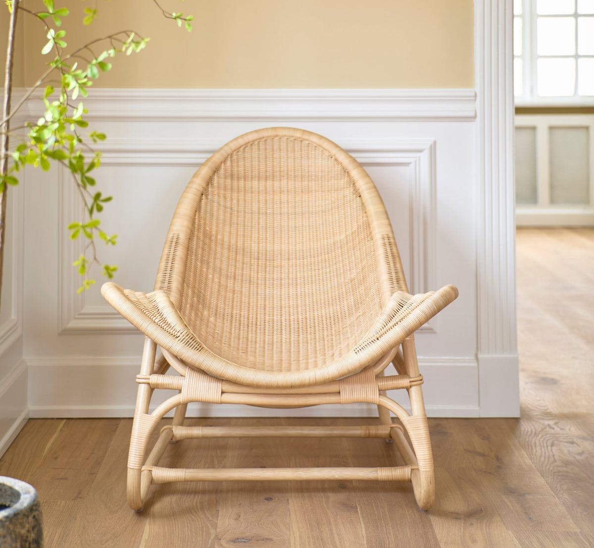 Dette er et livsstilsbillede af Pacifique Lænestol i natural core weave rattan frame. Set forfra ved hvide panelvægge.