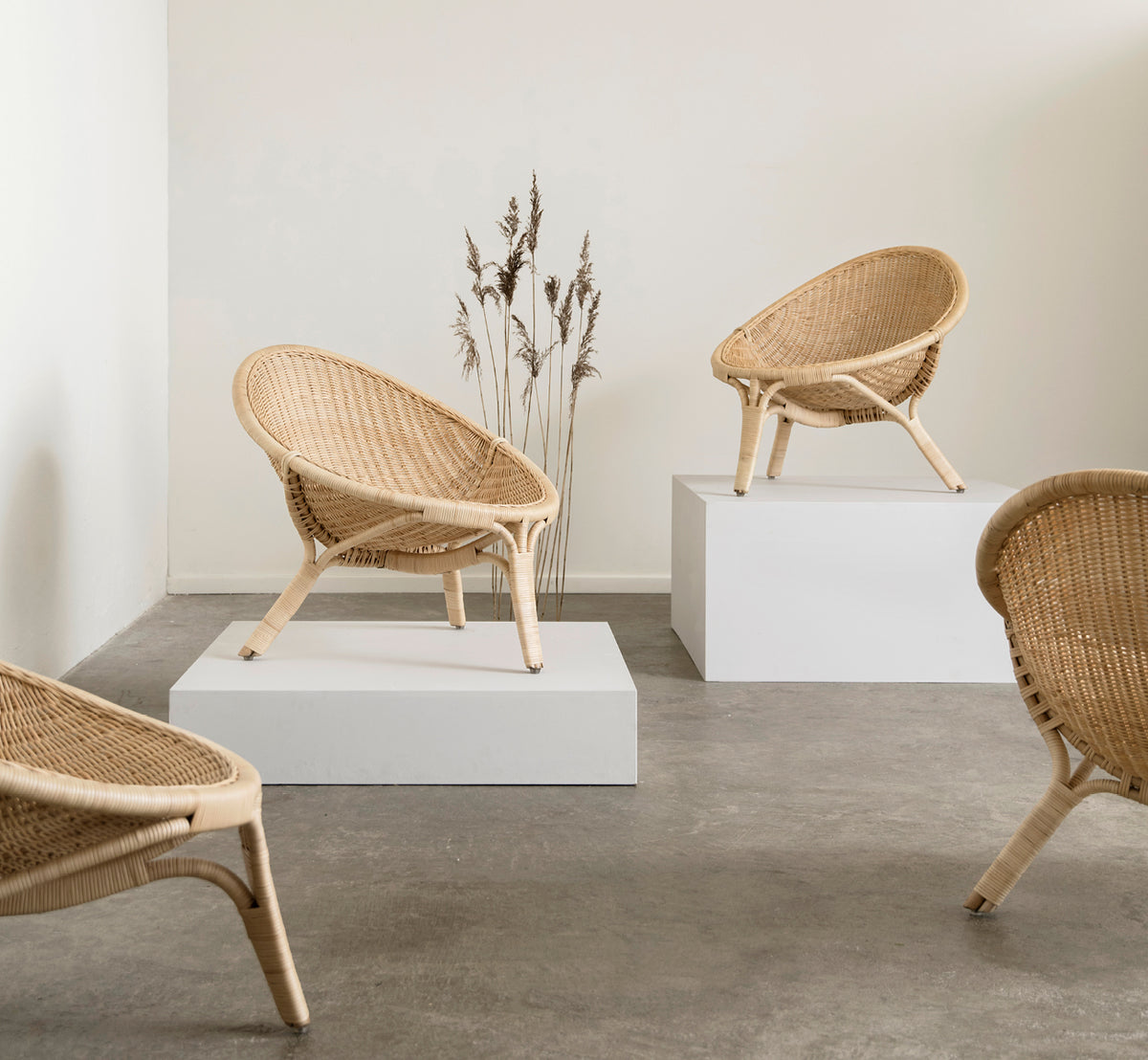 Dette er et livsstilsbillede af Rana Lænestol i natural core weave rattan frame. Stående alene i et rum med forgyldt panel og parketgulv.