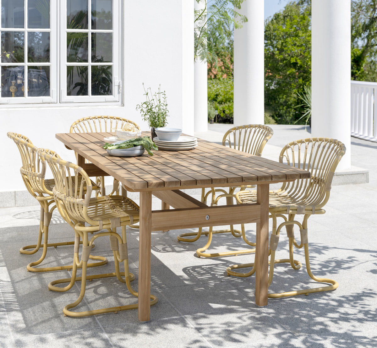 Dette er et livsstilsbillede af Rita Udendørs spisebordsstol i natural aluminium artfibre. Kombineret med et bistrobord på en hvid kolonneterrasse.
