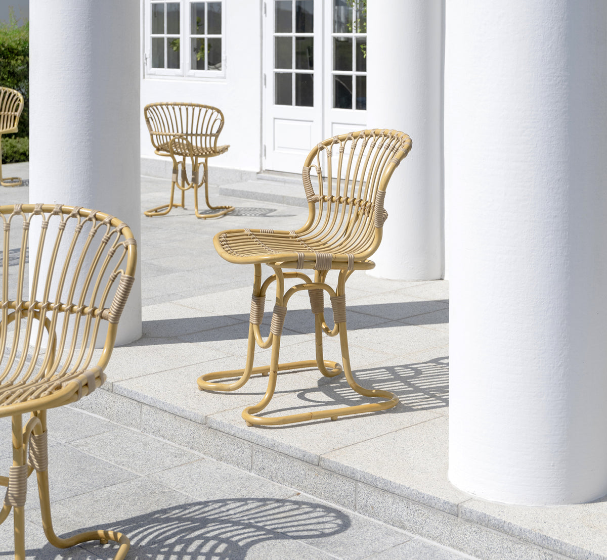 Dette er et livsstilsbillede af Rita Udendørs spisebordsstol i natural aluminium artfibre. Kombineret med et bistrobord på en hvid kolonneterrasse.