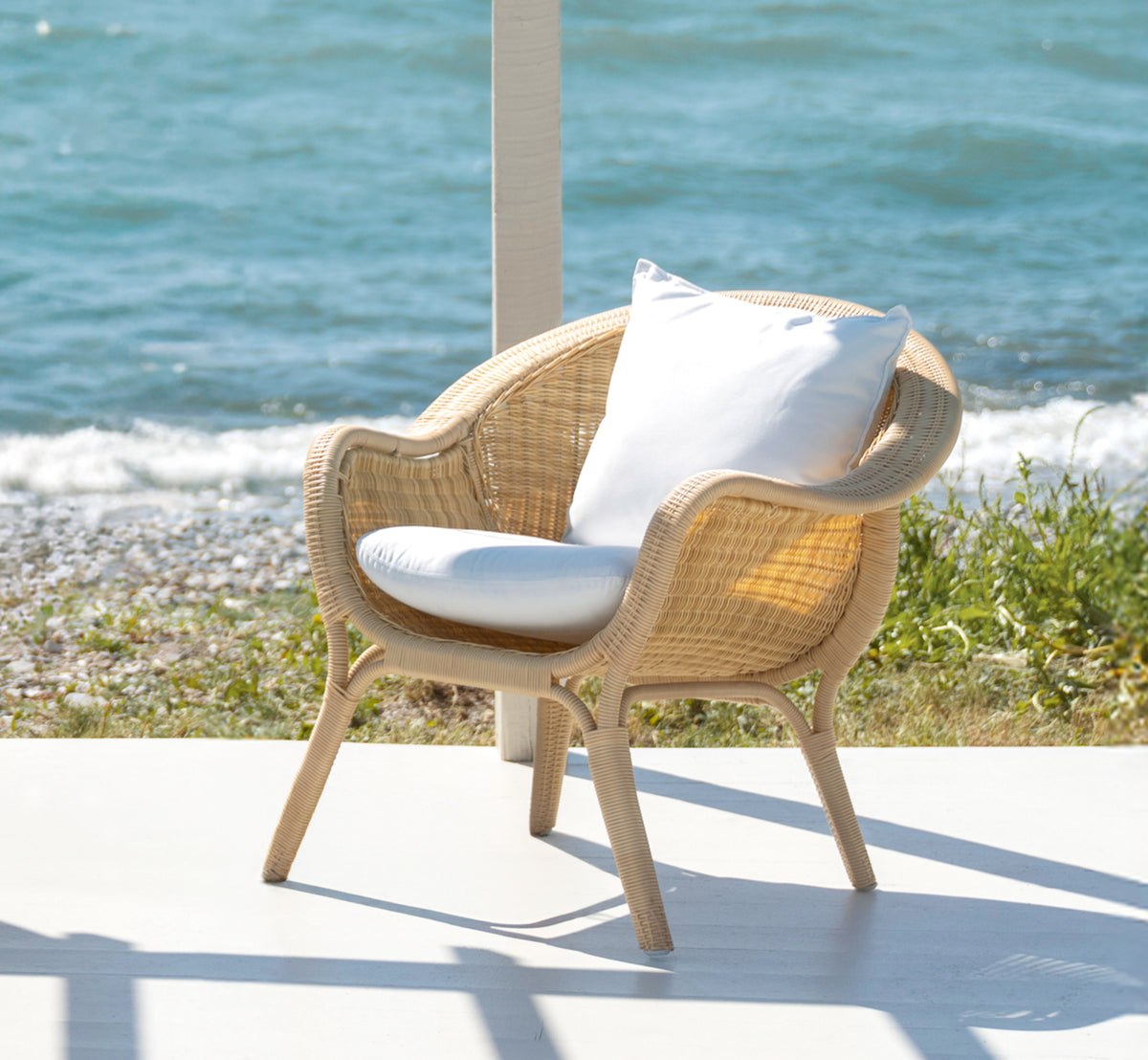 Dette er et livsstilsbillede af Madame Lænestol i natural core weave ArtFibre Aluminium, på en åben kystterrasse ved solnedgang med havudsigt og.