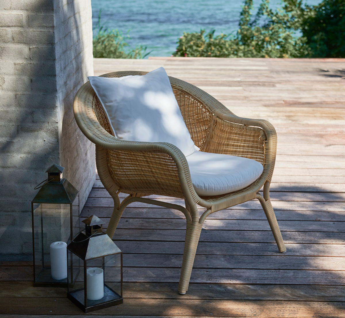 Dette er et livsstilsbillede af Madame Lænestol i natural core weave ArtFibre Aluminium, på en åben kystterrasse ved solnedgang med havudsigt og.