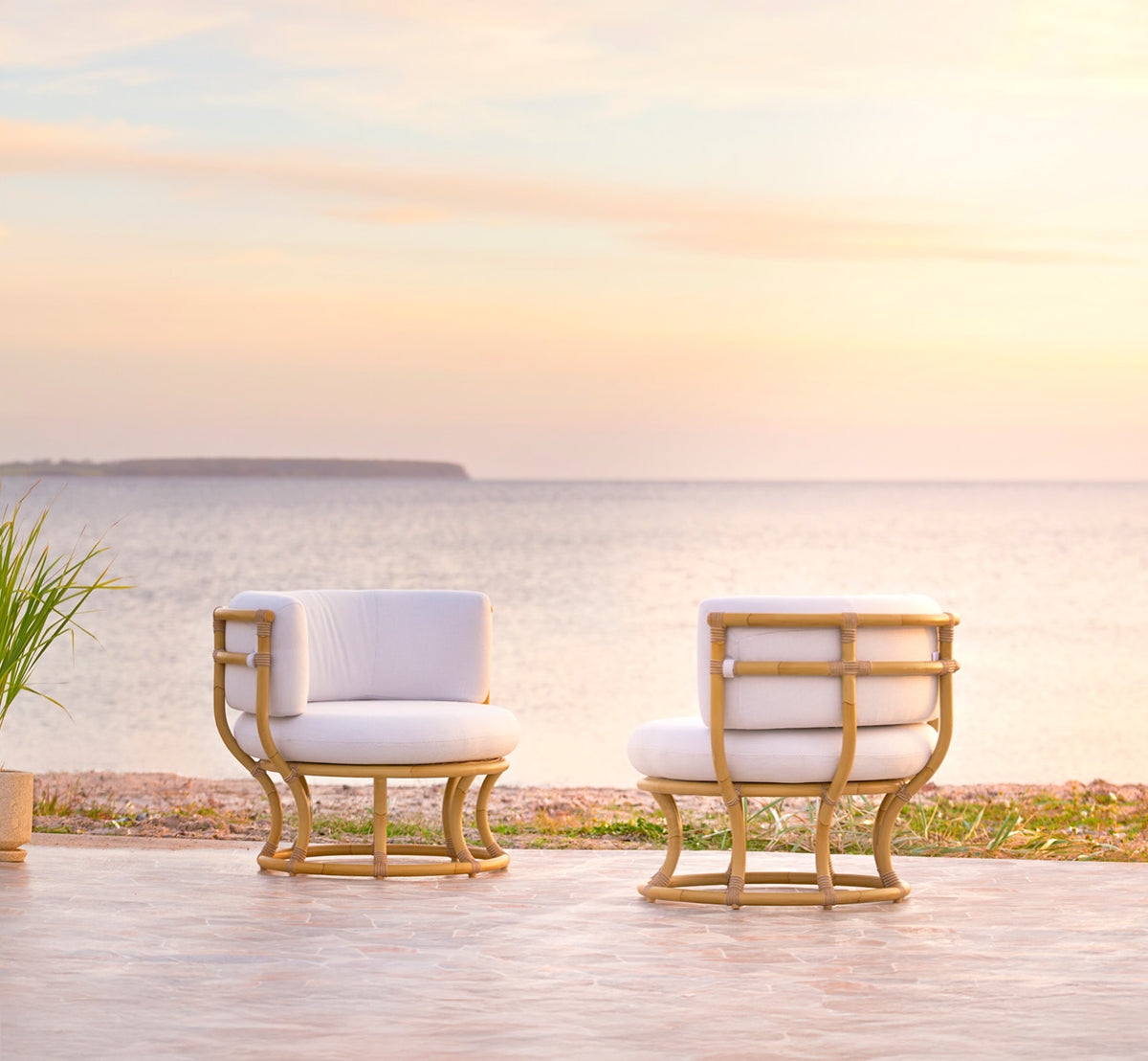 Dette er et livsstilsbillede af Coco Udendørs lænestol i natural Aluminium ArtFibre, på en åben kystterrasse ved solnedgang med havudsigt.