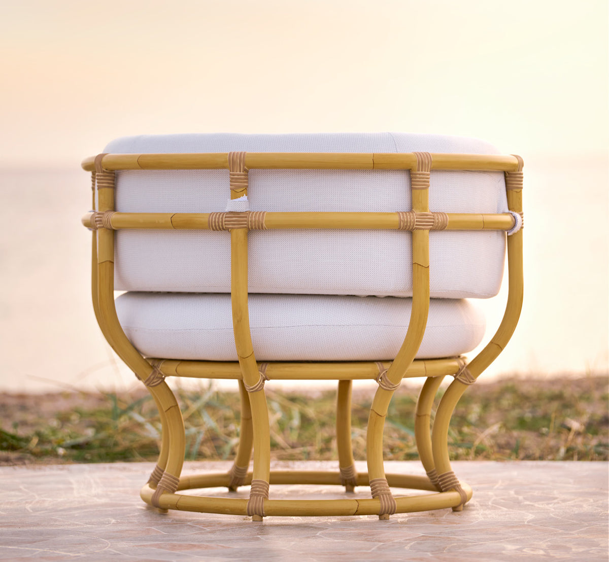 Dette er et livsstilsbillede af Coco Udendørs lænestol i natural Aluminium ArtFibre, på en åben kystterrasse ved solnedgang med havudsigt.