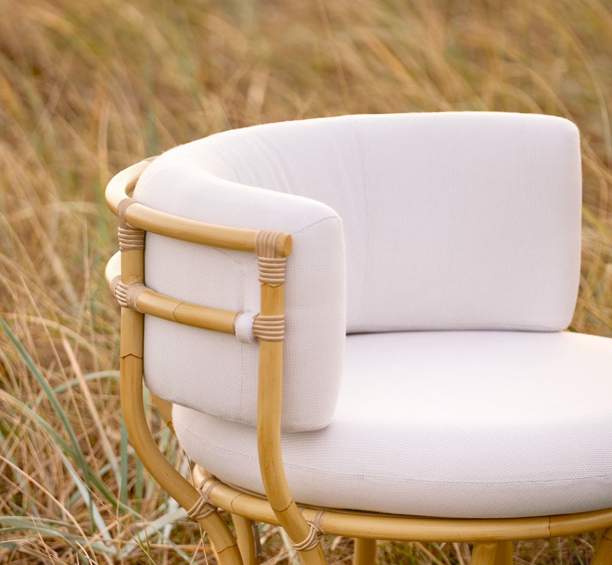 Dette er et livsstilsbillede af Coco Udendørs lænestol i natural Aluminium ArtFibre, på en åben kystterrasse ved solnedgang med havudsigt.