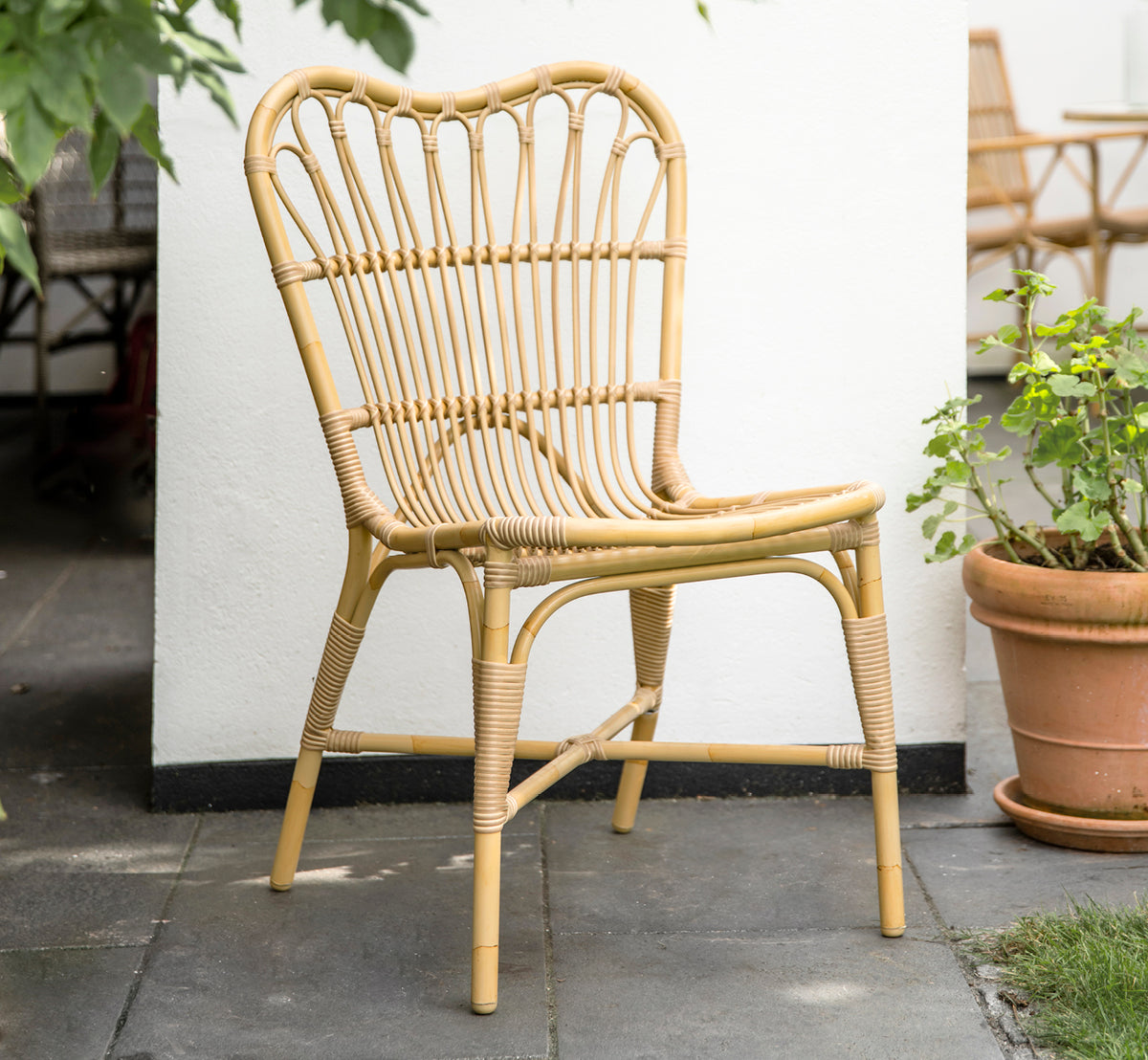 Dette er et livsstilsbillede af Margret Udendørs spisebordsstol i natural aluminium artfibre. Hvid gårdhave med terrakottakrukker og planter.