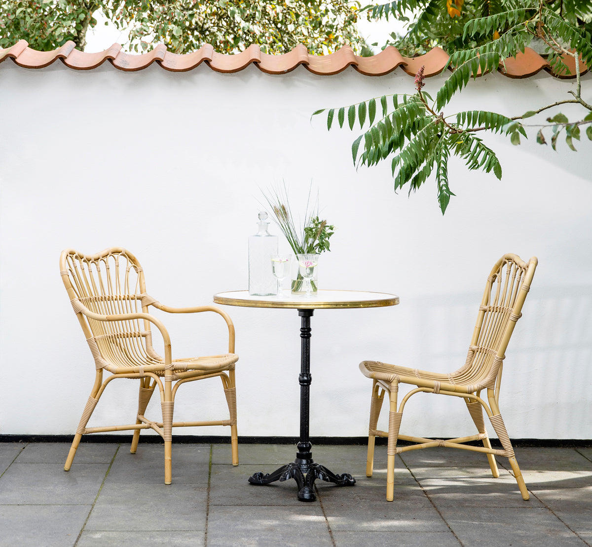 Dette er et livsstilsbillede af Margret Udendørs spisestuelænestol i natural aluminium artfibre. Gårdhave med cafébord under tegltagsudhæng.