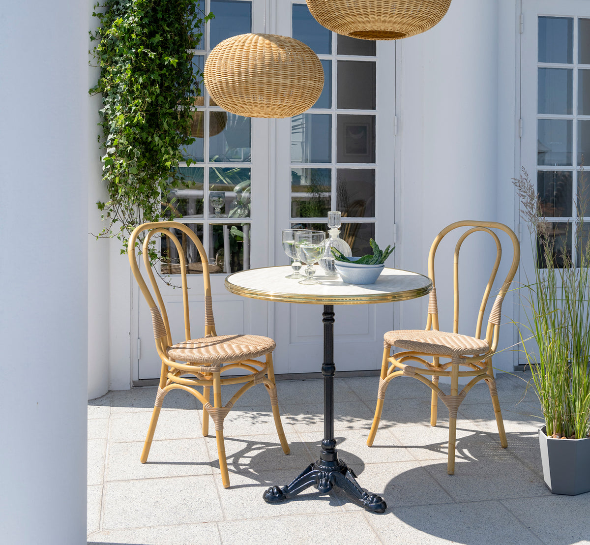 Dette er et livsstilsbillede af Lulu Udendørs spisebordsstol i natural aluminium artfibre. På en hvid terrasse med et cafébord og klatreplanter.