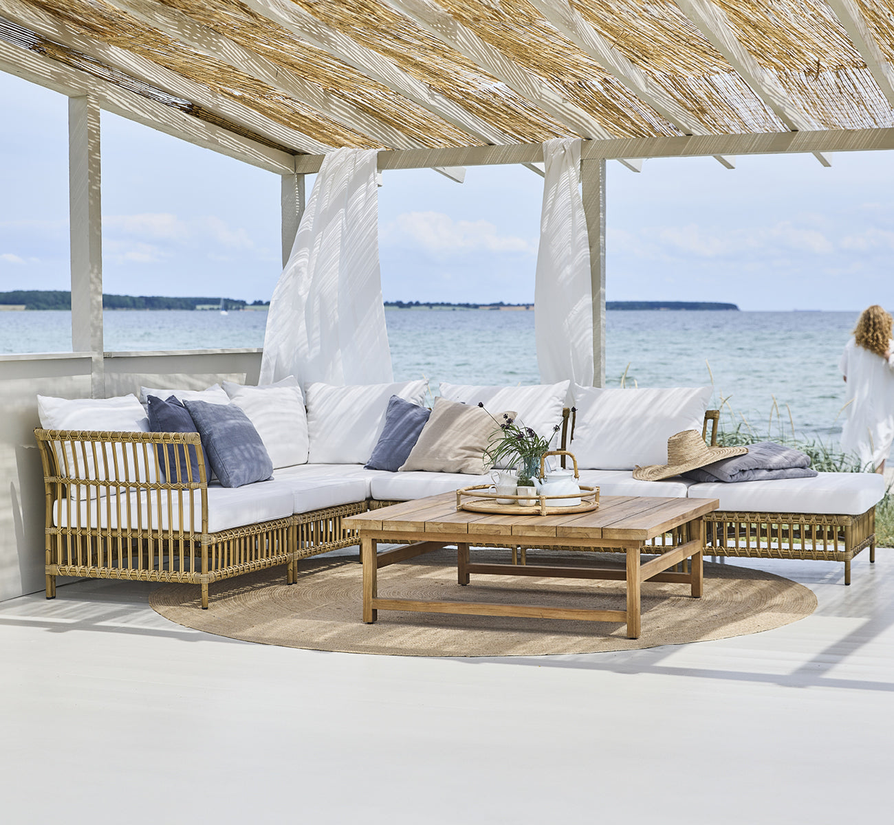 Dette er et livsstilsbillede af Maggie Sofa Centermodul i antique aluminium artfibre. Strandpavillon med modulsofa og havudsigt.