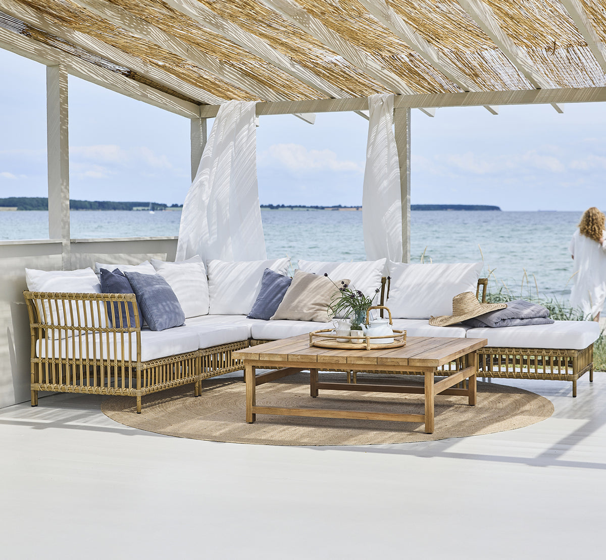 Dette er et livsstilsbillede af Maggie Sofa Centermodul i antique aluminium artfibre. Strandpavillon med modulsofa og havudsigt.
