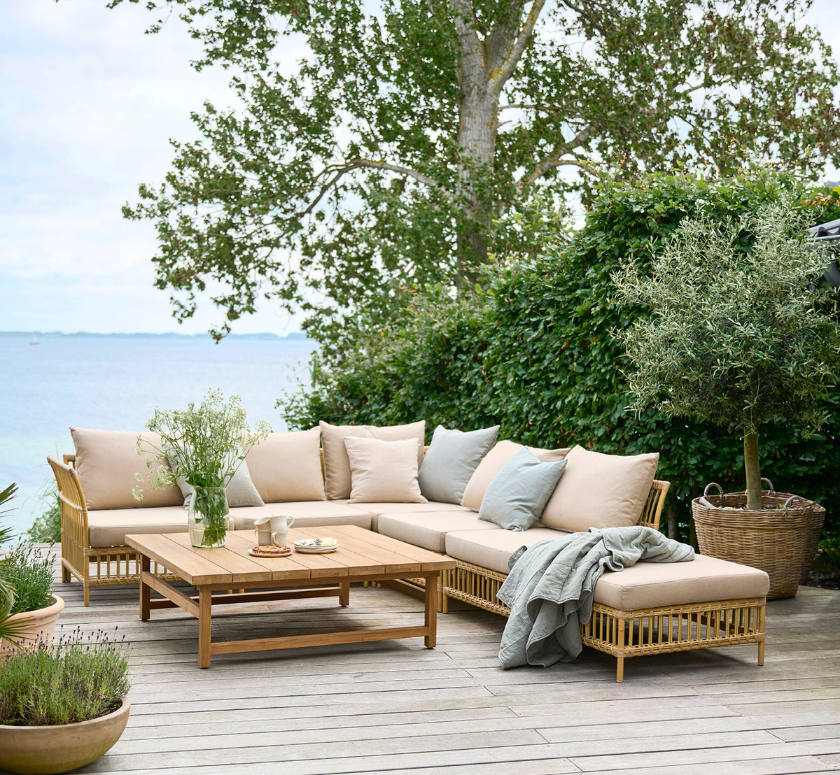 Dette er et livsstilsbillede af Maggie Sofa Puf Modul m. Glas i natural aluminium artfibre. Dæk ved havet med modulsofa og draperet tæppe.