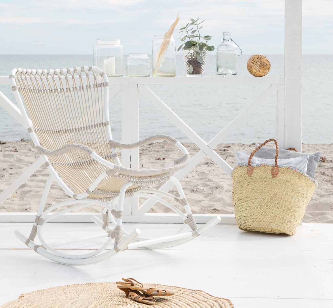 Dette er et livsstilsbillede af Monet Exterior Rocking Chair i dove white aluminium artfibre. I en strandpavillon med havudsigt.