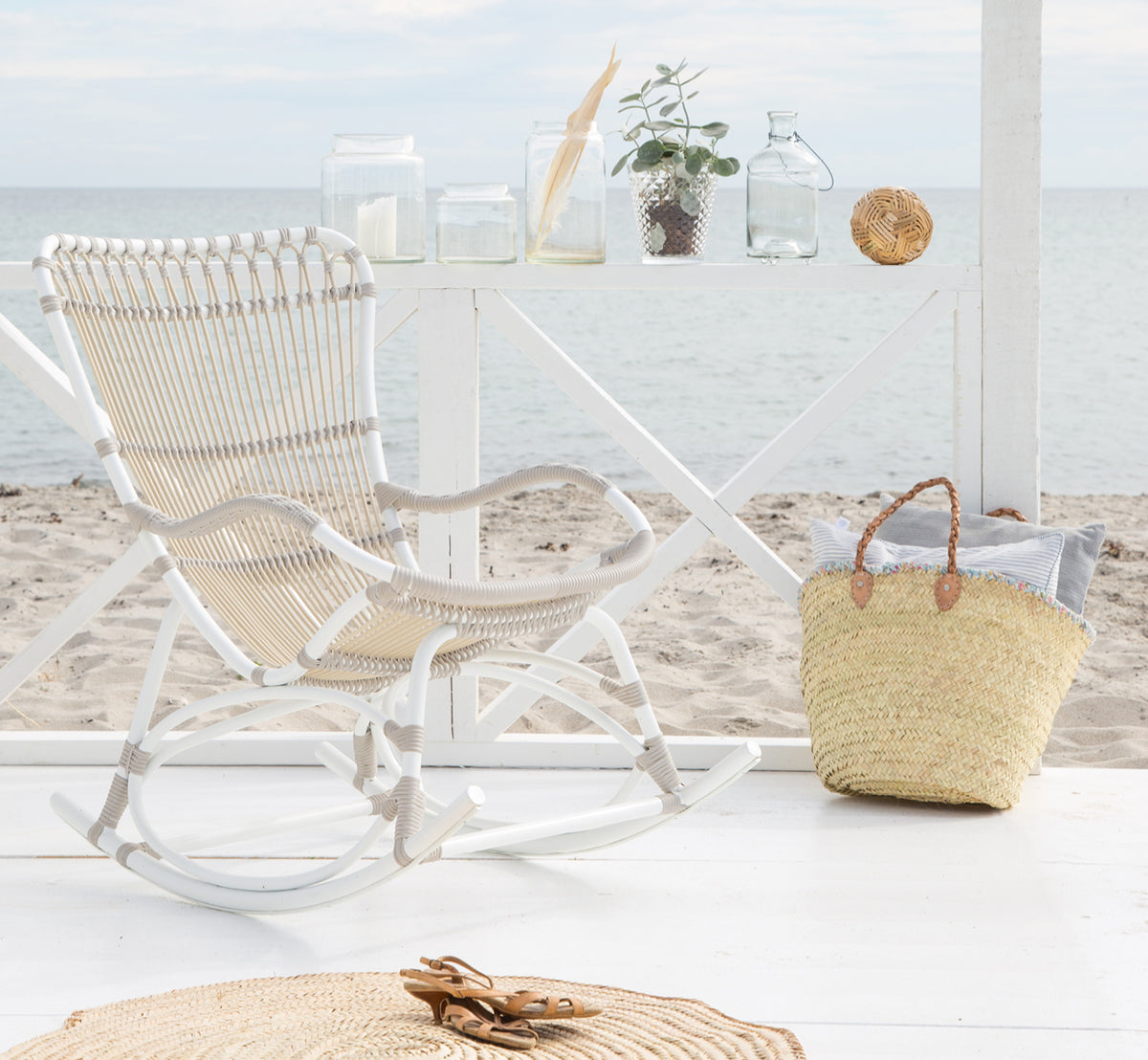 Dette er et livsstilsbillede af Monet Exterior Rocking Chair i dove white aluminium artfibre. I en strandpavillon med havudsigt.