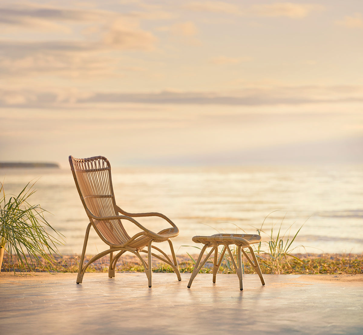 Dette er et livsstilsbillede af Monet Exterior Lounge Chair i antique aluminium artfibre. I en strandpavillon med hvide gardiner.