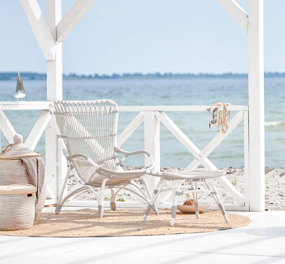 Dette er et livsstilsbillede af Monet Exterior Lounge Chair i dove white aluminium artfibre. I en strandpavillon med jutetæppe.