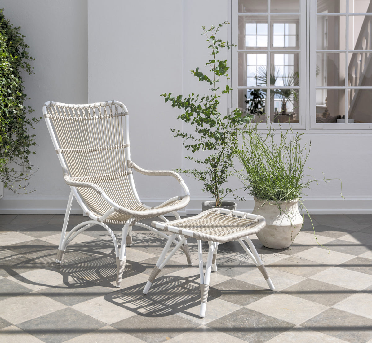Dette er et livsstilsbillede af Monet Exterior Footstool i dove white aluminium artfibre. På en strandveranda med lænestol.