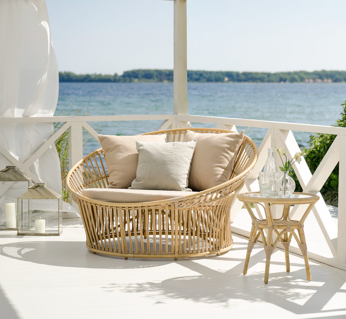 Dette er et livsstilsbillede af Olympia Nest Exterior i natural aluminium artfibre. I en strandpavillon med linnedpuder.