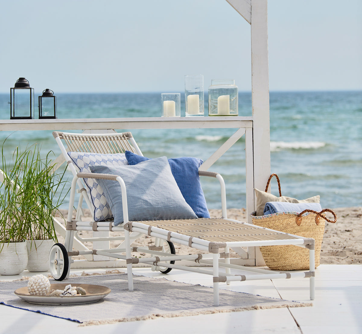 Dette er et livsstilsbillede af Josephine Solseng i dove White aluminium artfibre, på et hvidt trædæk ved stranden under en hvid pergola med.